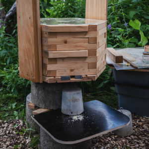 Moderni mehiläispesä: kuusikulmaisista puulevyistä koostuva rakennelma, läpinäkyvästä plexilasista tehty kansi, jossa reikiä.