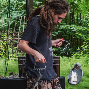 Mies jolla pitkät rasta-letit soittaa omatekoisia, jätemateriaalista tehtyjä soittimia.