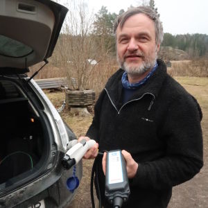 Bilen går att ladda i ett vanligt vägguttag. Kurt Andersson intill sin bil med bilens laddningskabel i handen.