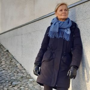Vi har lågikomsttagare bland de anställda: hälso- undervisnings- och dagvårdssidan så visst är sjukvårdsservicen vi ger en förmån. Det kan kosta mycket annars eller vara långa köer, säger Lena Meyer på Företagshälsan Helsingfors. Lena Meyer fotad utomhus lutad mot en husvägg.
