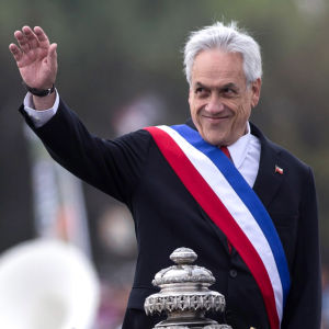 Demonstranterna kräver att president Piñera avgår. Bilden är tagen under en militärparad 19.7 2019. Chiles president ler och ser åt sidan. Hans hand är utsträckt eftersom han hälsar.