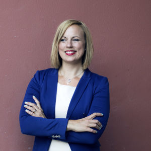 Blond leende kvinna i halvbild mot en pink vägg.