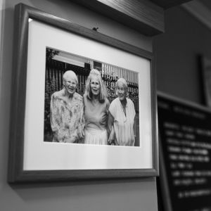 Nick Victorzon beundrar matlagningskunskaperna hos släktens damer, det vill säga mammas faster, mamma och mormor. Svartvitt foto av Nick Victorzons mamma, mammas faster och mormor på restaurangväggen.