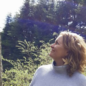 Johanna Sandberg hoppas på mer regional jämlikhet om en nationell e-bibba blir verklighet. Johanna Sandberg står i profil och tittar uppåt mot träd och himmel.