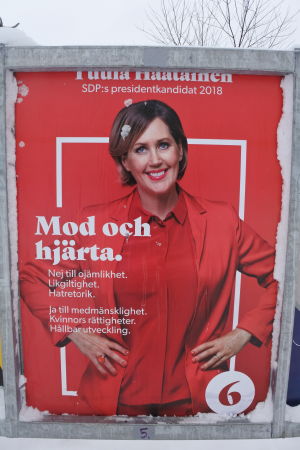 tuula haatainens valaffisch. hon har röda kläder och står mot en röd bakgrund.