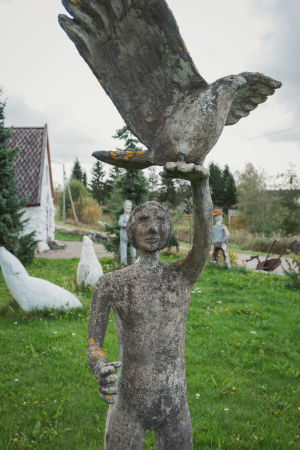 Lintua kädellään pitelevä ihmistä esittävä patsas, taustalla muita patsaita ja valkoinen, pieni kirkko