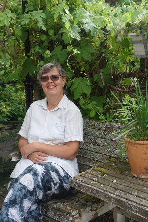Catharina Hanstén är trädgårdsmästare och biolog. En dam sitter på en bänk ute i en trädgård och ler.