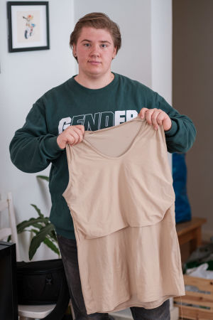 Ricky visar upp sin binder, ett klädesplagg som används av många transpersoner. Bindern plattar till brösten, tar bort feminina kurvor vid midjan och ger en mera maskulin kropp. en ung transperson visar upp ett klädesplagg som transpersoner använder för att platta till sina bröst.