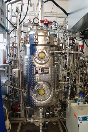 Solar Foods enögda, bubblande minion Bild inifrån ett laboratorium. I mitten står en bioreaktor, den är gjord i blänkande metall och har rör och slangar som går in i den cylindriska kroppen.