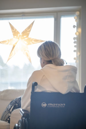 "Jag fick ett erbjudande om en assistent kring nyåret, det var strax efter att en av mina bekanta gjort en orosanmälan om mig till staden. Jag måste ändå tacka nej eftersom assistenten inte hade körkort", säger Tuija Wahalahti. En kvinna sitter i en rullstol framför ett fönster. I fönstret står en julstjärna.