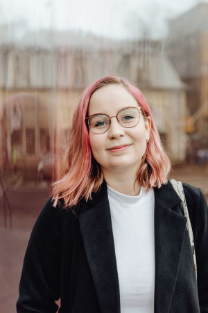 Evelina Blom studerar engelska i Åbo. Evelina Blom, en flicka med rödaktigt hår, glasögon och svart kavaj, tittar rakt in i kameran.