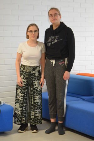 Sara Hukkataival och Ella Sundell går i åttonde klass i Kasavuoren koulu. De har gått i språkbad ända sedan förskolan. Bild på språkbadseleverna Sara och Ella som poserar bredvid varandra i skolkorridoren.