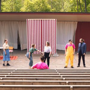 Teaterövningar i Tenala. Folk på utomhusscenen och några människor som sitter på läktaren.