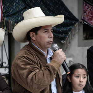 Presidentknidaten Pedro Castillo står  bakom ett bord och talar i en mikrofon. Bredvid honom står en rad män och kvinnor och ett barn.