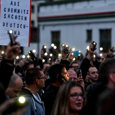 Demonstranter i Chemnitz håller upp upplysta mobiltelefonskärmar i kvällsmörkret.