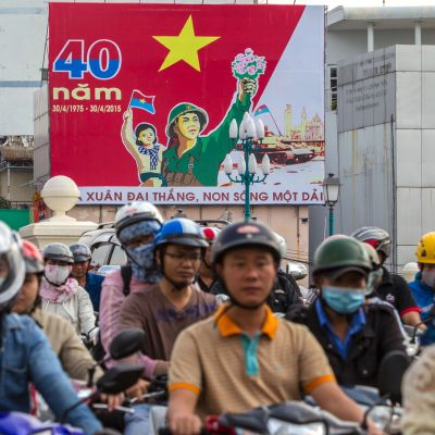 Ihmiset ajavat Vietnamin sodan päättymistä 40-vuotta sitten juhlistavan kyltin ohi Ho Chi Minhissa.