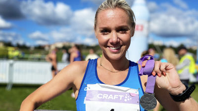 Nina Chydenius poserar med en present i ena handen och en medalj i den andra. Hon ler.