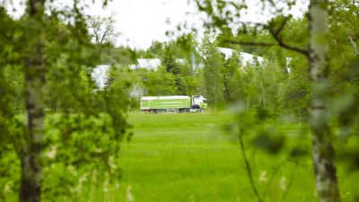 En bil som transporterar avloppsslam vid ett gräsfält. Vid fältet finns träd.