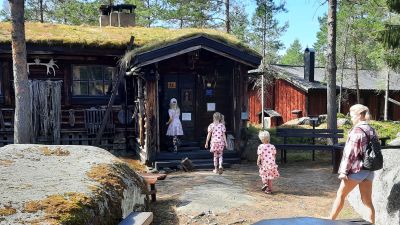 Barn och en kvinna som går mot ett timrat hus.
