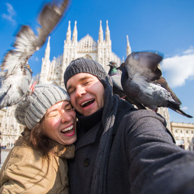 man och kvinna tar ett självporträtt, skrattar då de attackeras av duvor