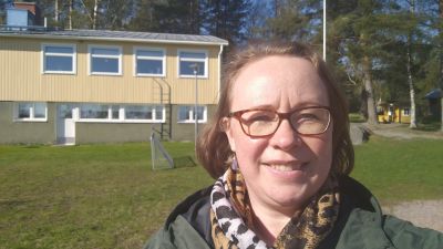 Kvinna ler mot kameran framför ett gult hus.