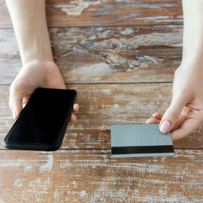 Händer som håller i en smarttelefon och ett bankkort.