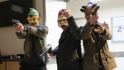 Tre män med masker som föreställer en julgubbe, tomte och en ren rusar in genom en dörr med dragna vapen.