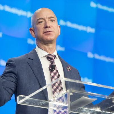 Jeff Bezos bakom genomskinlig talarstol med utsträckta händer
