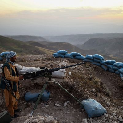 En turbanförsedd milisman står bakom en maskingevär i bergig terräng