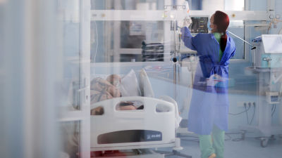 En sjukskötare i skyddsutrustning vårdar en sängliggande coronapatient på intensivvårdsavdelning.