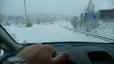 Hand som håller i bilens ratt, snöig väg.
