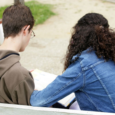 En bild på två personer som läser från ett papper. Vi ser bara personernas ryggar - den ena är en kvinna med lockigt hår och den andra en man 