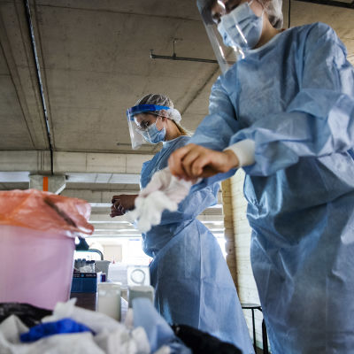 Två sjukskötare klädda i blå skyddsdräkt tar av sig sina handskar vid en coronatestningspunkt.