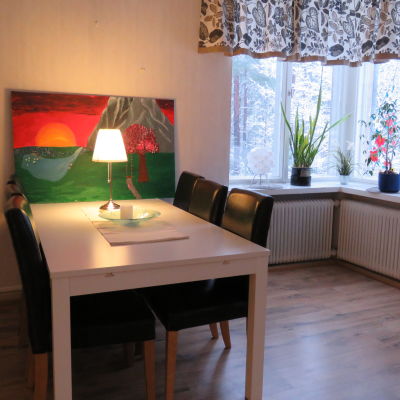 ett rum med matbord, stolar och en färggrann tavla som står på bordet och lutar mot väggen. Ett fönster med pålistrade dekaler (fjärilar och blommor)