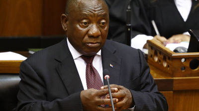 Sydafrikas president Cyril Ramaphosa, klädd i kostym, sitter i parlamentet och stirrar tomt framför sig med händerna knäppta.