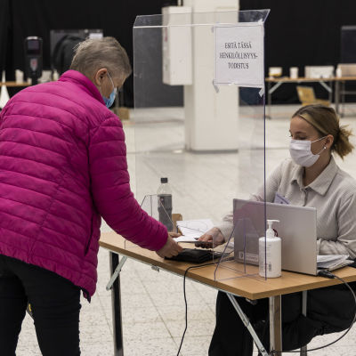 En äldre kvinna visar ID till en valfunktionär i samband med förhandsröstning i välfärdsområdesvalet.