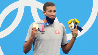 Ahmed Hafnaoui poserar med guldmedalj och blommor.