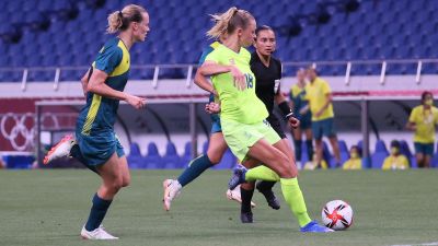 Fridolina Rolfö skjuter i väg bollen, omgiven av två australiska spelare.