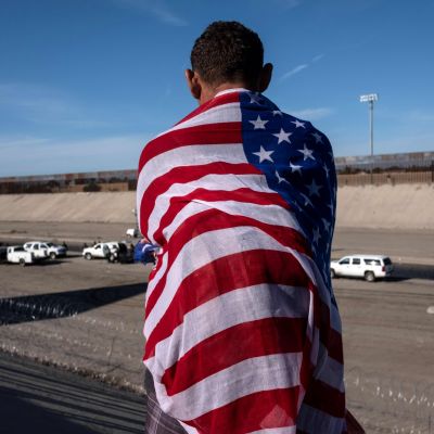 En centralamerikansk migrant insvept i USA:s flagga ser ut över Tijuana-flodens så gott som torra flodbädd på den mexikanska sidan om en gränsövergång mot USA. Bilden är tagen 25.11.2018.