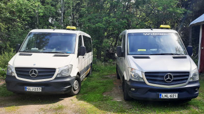 Två stora taxibilar bredvid varandra på en gård.