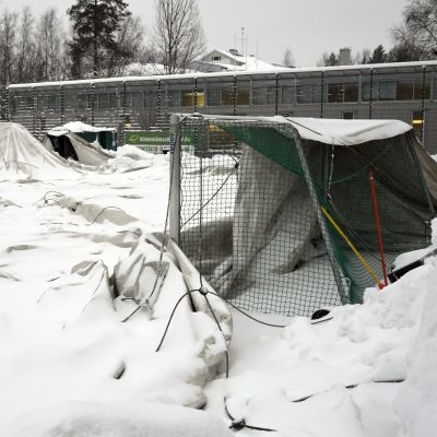 Taket på en uppblåsbar idrottshall ligger på marken , täckt av snö. Till höger syns ett mål.