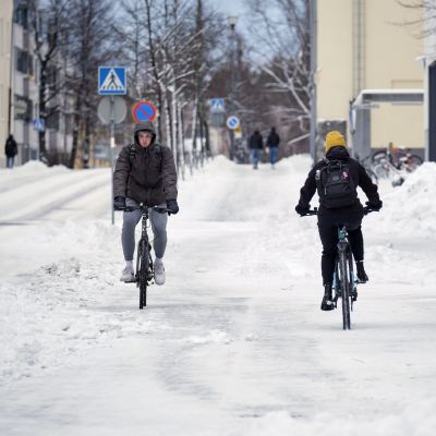 Kaksi pyöräilijää lumisella kadulla.