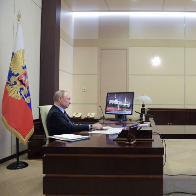 President Vladimir Putin sitter vid ett skrivbord och ser på en tv-skärm. 