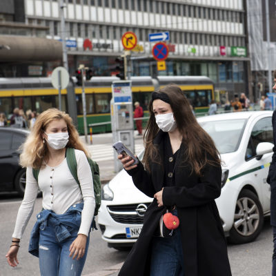 Två unga kvinnor med munskydd promenerar i centrum av Helsingfors.