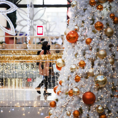 Kasvomaskiin pukeutunut nuori kävelee joulukoristeilla koristellussa ostoskeskuksessa.