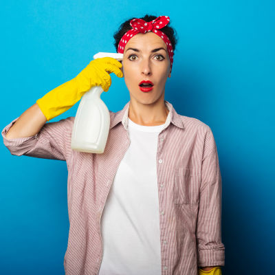 Kvinna med städutrustning riktar tvättmedelsflaska mot tinningen 