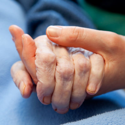 En yngre person håller en äldre person i handen.