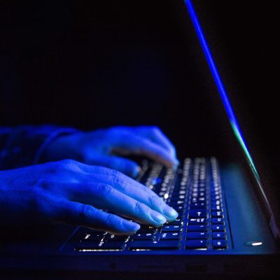 Närbild på en laptop. På tangentbordet är två händer som lyses blåa av skenet från skärmen.