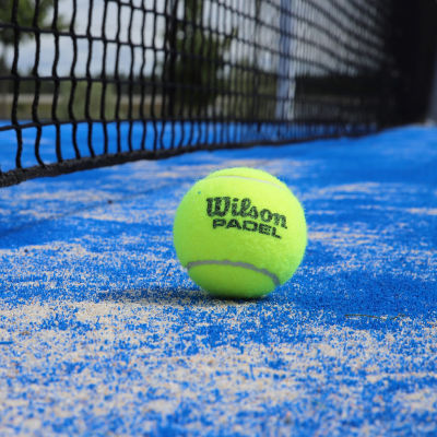 En grön padelboll bredvid ett nät på en blå spelplan.