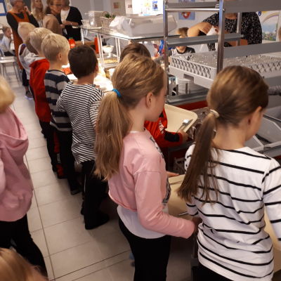 Barn i kö till skollunchen i en matsal.